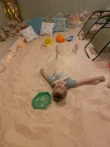 Child laying in salt with beach toys